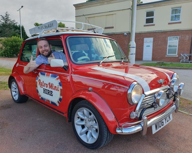 a man giving thumbs up out the window of a classic red mini cooper on a self drive road trip