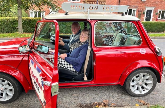 a man and a woman sitting inside a classic red mini cooper ready to go on a self drive road trip