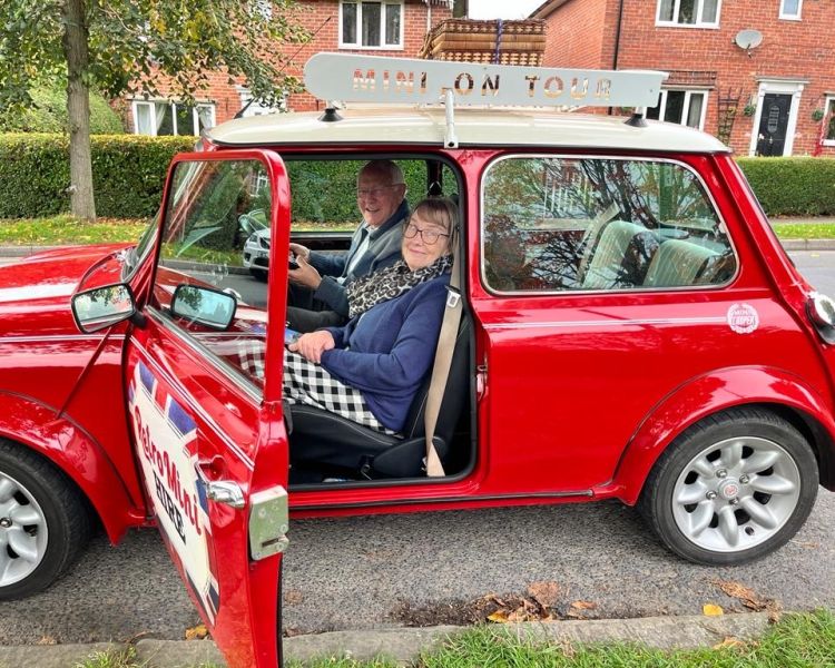 a man and a woman sitting inside a classic red mini cooper ready to go on a self drive road trip
