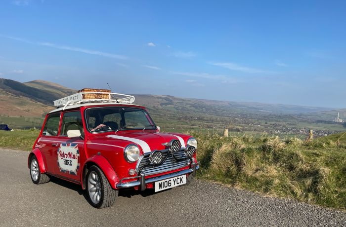 a classic red mini cooper parked up in front of countryside views on a self drive road trip