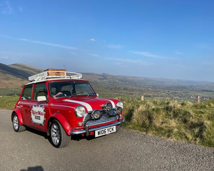 a classic red mini cooper parked up in front of countryside views on a self drive road trip