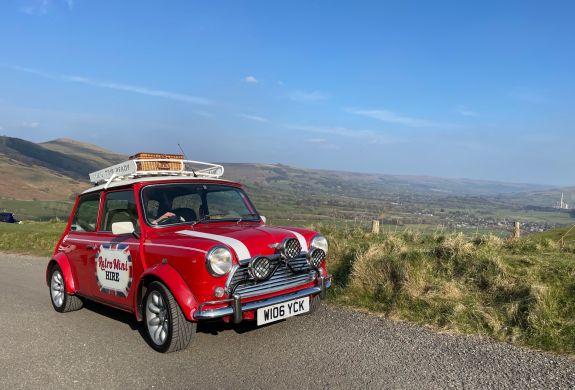 a classic red mini cooper parked up in front of countryside views on a self drive road trip