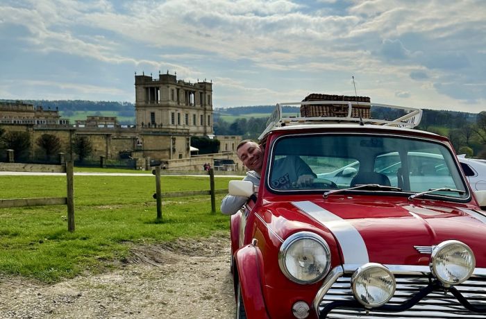 a man poking his head out of the window of a red classic mini cooper parked up outside chatsworth house