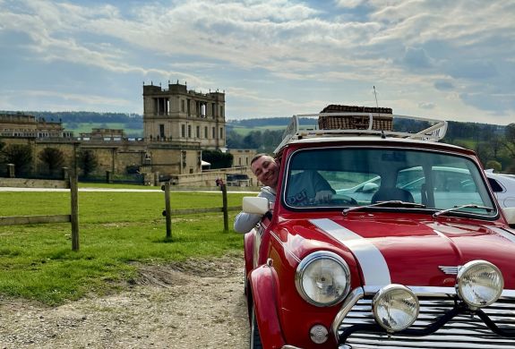a man poking his head out of the window of a red classic mini cooper parked up outside chatsworth house