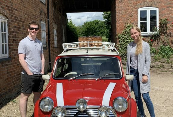 a man and a woman standing either side of a red classic mini cooper ready for a hire and drive experience