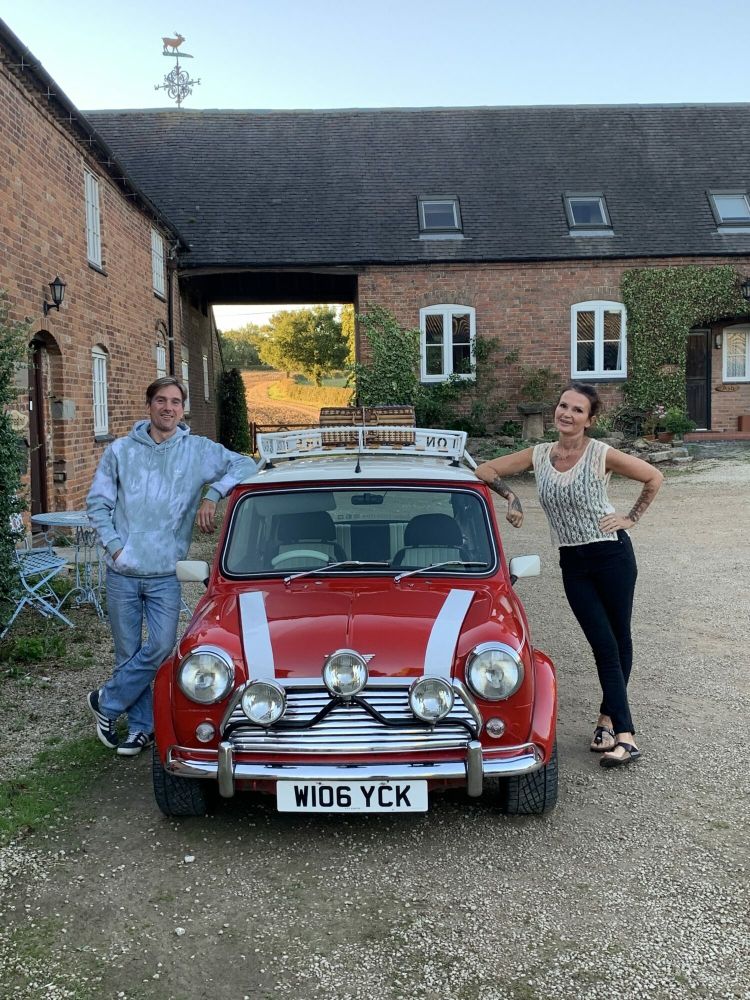 a man and a woman standing either side of a red classic mini cooper on a hire and drive experience