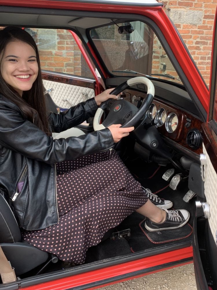 a woman sitting in the drivers seat of a classic red mini cooper on a hire and drive experience