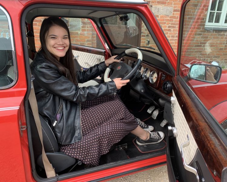 a woman sitting in the drivers seat of a classic red mini cooper on a hire and drive experience