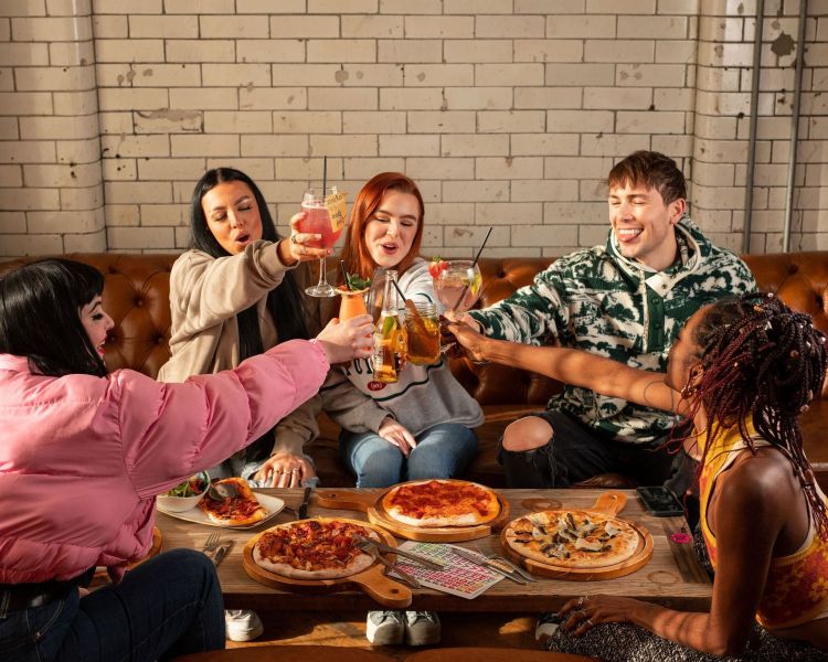 a group of 5 clinking drinks with pizza