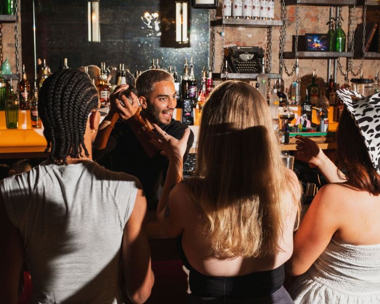 a bartender shaking cocktails while 3 guests watch