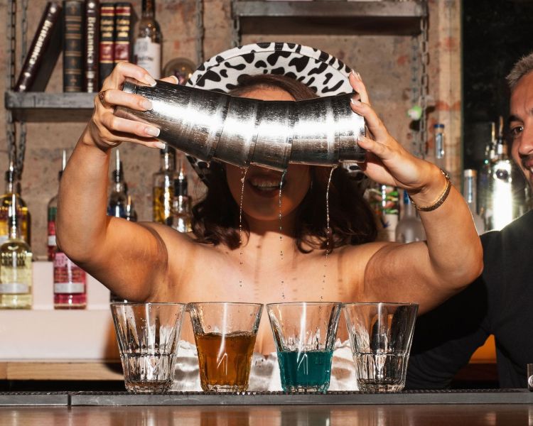 a lady wearing a cowboy hat pouring multi shots with a bartender observing