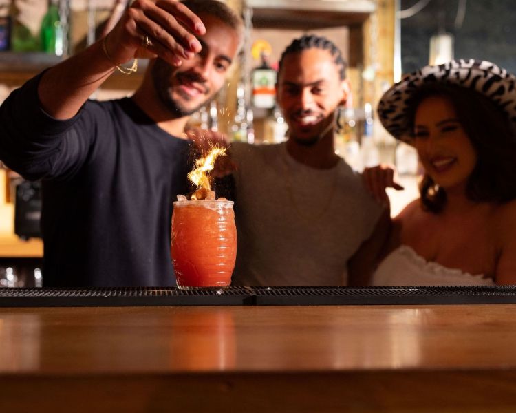a bartender adding final touches to a cocktail while a man and women look on in the background