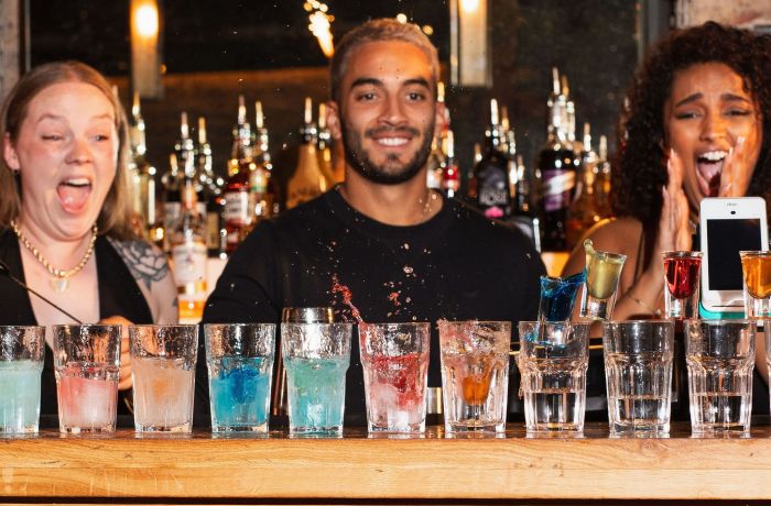 3 bartenders looking at a line of cocktails with excitement
