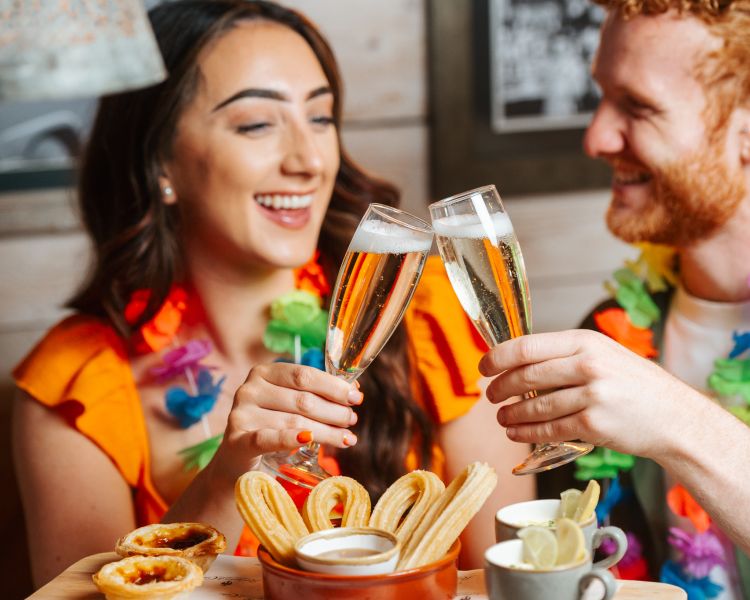 a man and a woman enjoying a glass of prosecco with cuban inspired afternoon tea