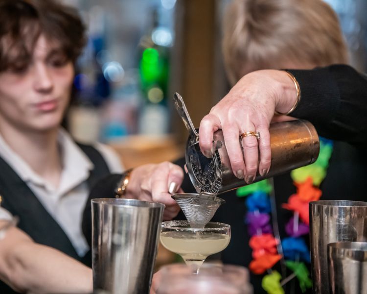 a woman pouring a cocktail into a glass through a strainer on a cocktail masterclass at revolucion de cuba