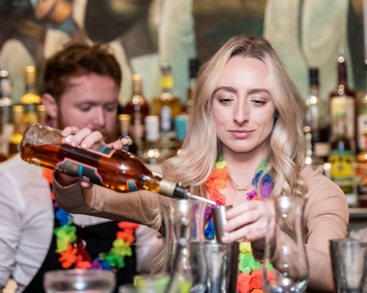 a woman pouring a spirit into a shot glass to make a cocktail on a cocktail masterclass at revolucion de cuba