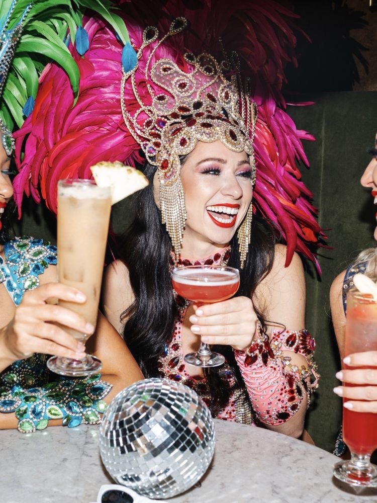 three ladies dressed in rio carnival dress enjoying cocktails at revolucion de cuba