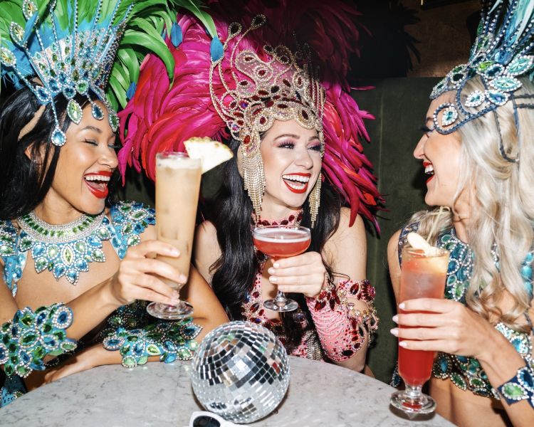 three ladies dressed in rio carnival dress enjoying cocktails at revolucion de cuba