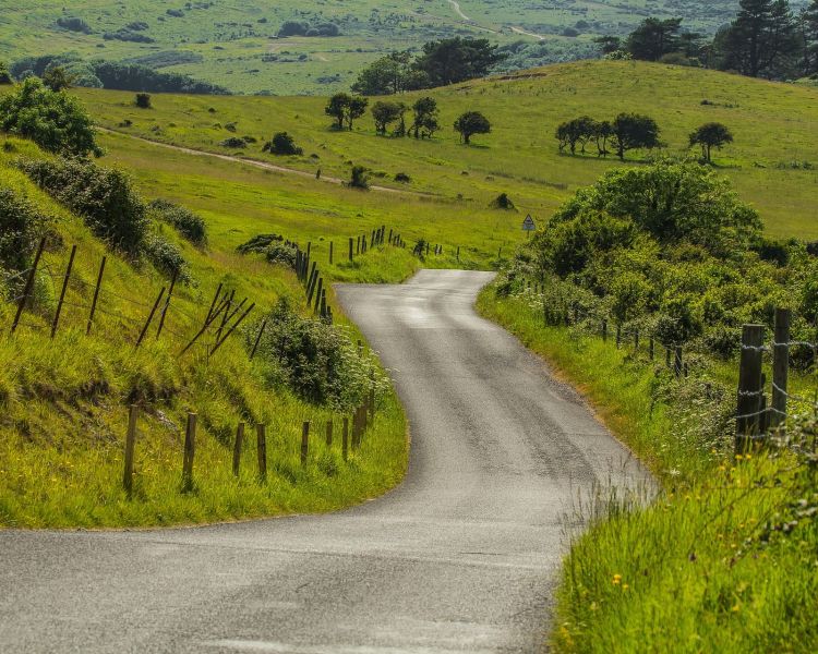 an open road through the peak district with green rolling hills in the background