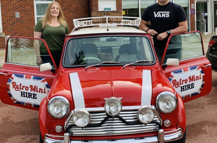 a man and a woman standing either side of a classic red mini cooper on a hire and drive experience day