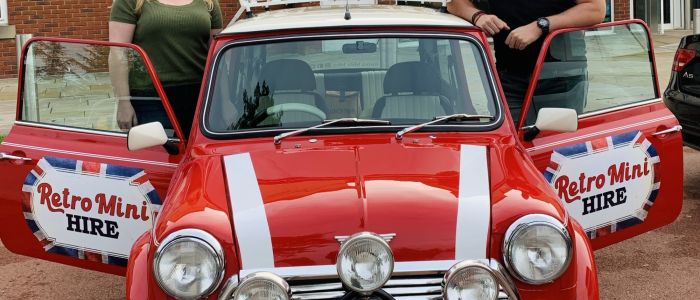 a man and a woman standing either side of a classic red mini cooper on a hire and drive experience day