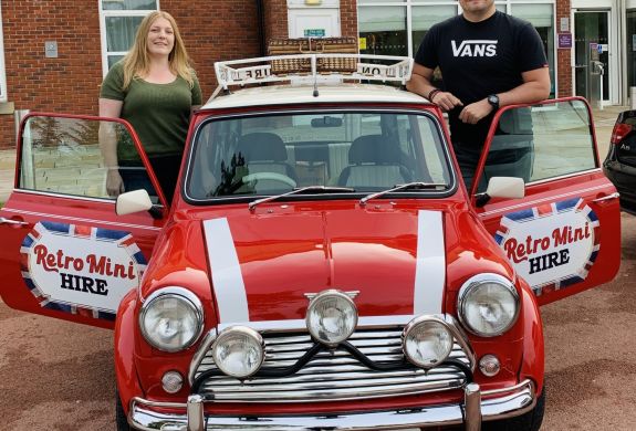 a man and a woman standing either side of a classic red mini cooper on a hire and drive experience day