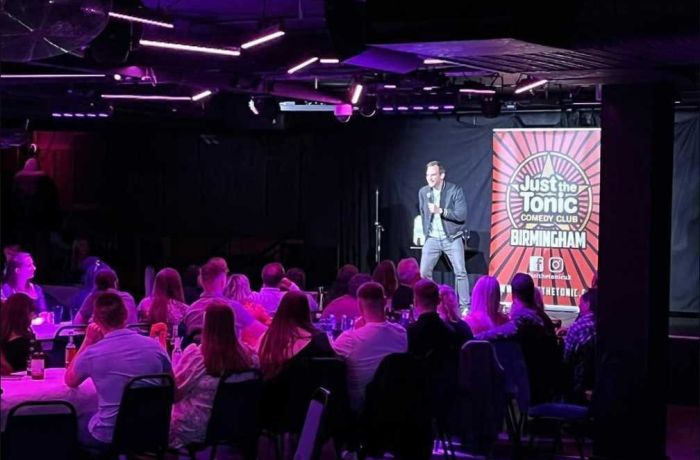 a comedian on stage with people looking on at a comedy night