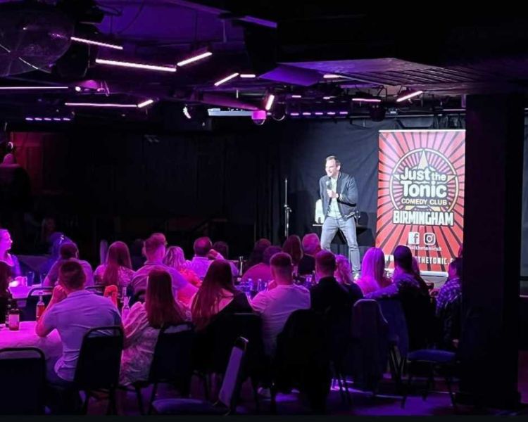 a comedian on stage with people looking on at a comedy night