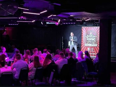 a comedian on stage with people looking on at a comedy night