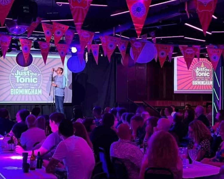 a comedian on stage with people looking on at a comedy night