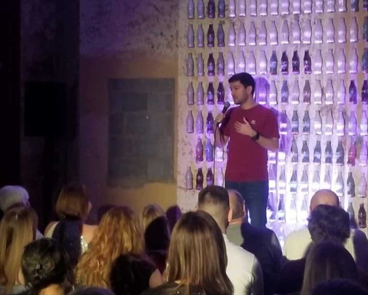 a comedian on stage with people looking on at a comedy night