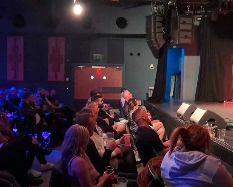a comedian on stage with people looking on at a comedy night