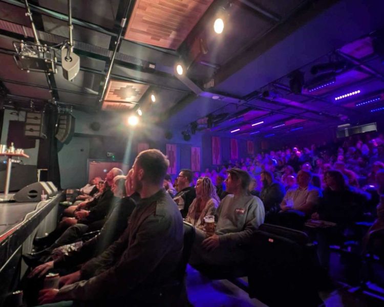 a comedian on stage with people looking on at a comedy night