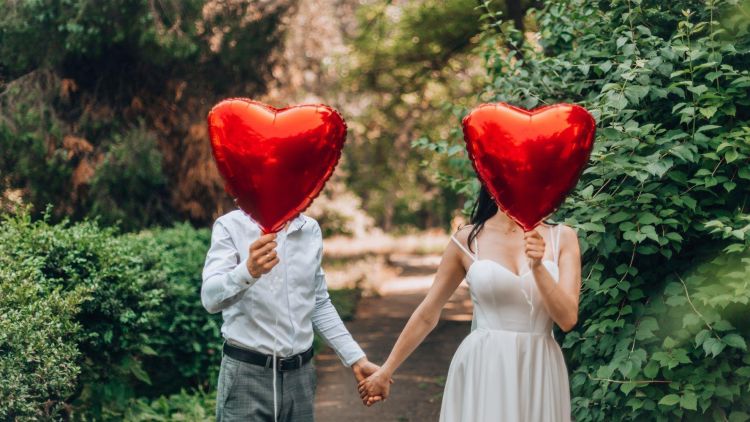 Man and woman hugging holding a red heart balloon over their faces