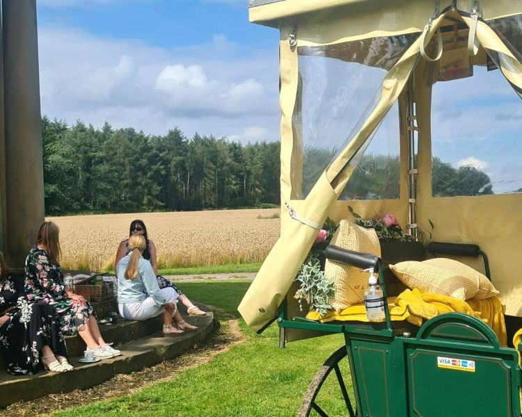people sitting to the side of a carriage outside in the countryside as part of a horse and carriage afternoon tea experience in yorkshire