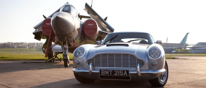 a british classic car next to an airplane on an airfield track