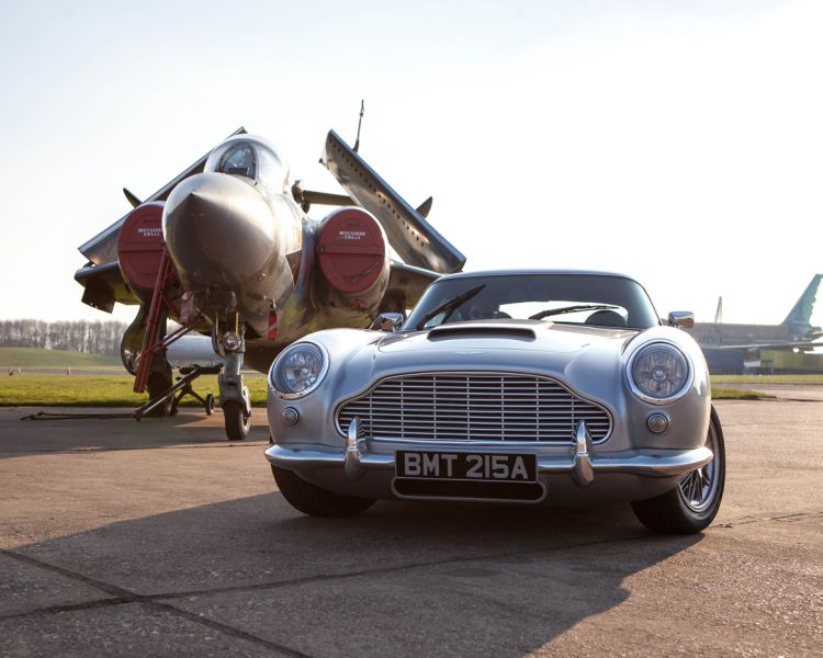a british classic car next to an airplane on an airfield track