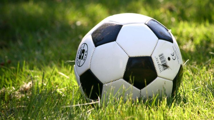 A black and white football on a football pitch inside a stadium