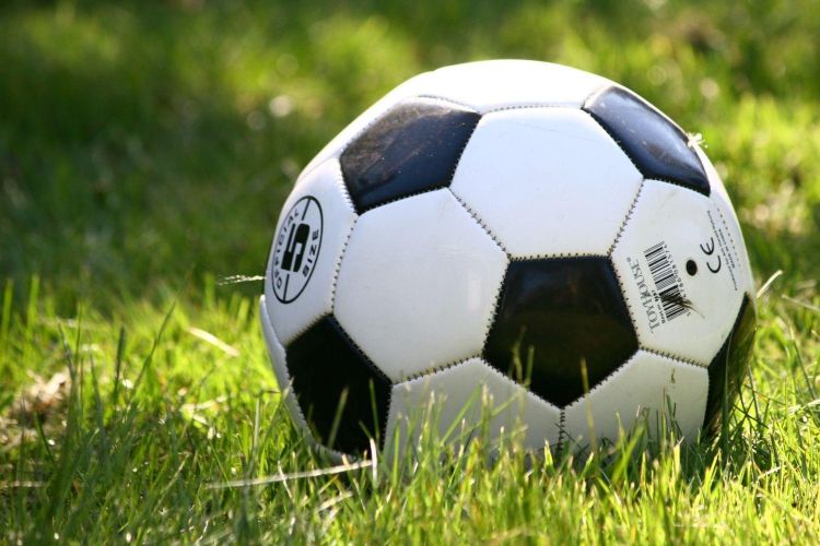 A black and white football on a football pitch inside a stadium