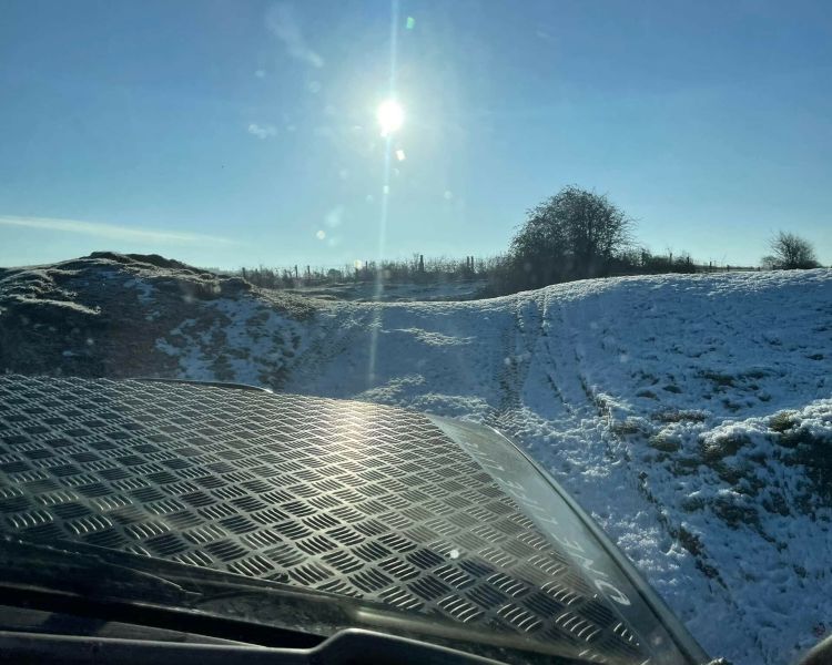 a photo taken through the windscreen of an off road vehicle looking out over snow covered ground with the sun shining as part of an off road driving experience