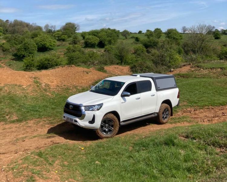 a white 4x4 vehicle driving on a muddy track in a field on a sunny day as part of an off road driving experience in Bristol