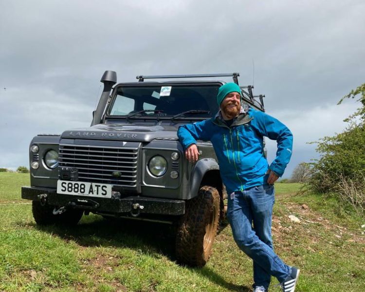 a man posing next to a land rover in a muddy field as part of an off road driving experience in Bristol