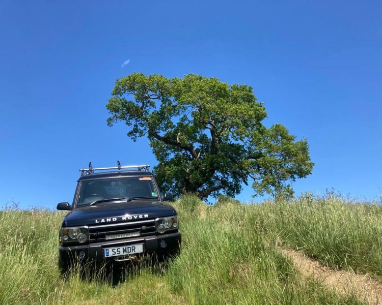 a black 4 x 4 land rover driving through a grassy field on a bright sunny day as part of a driving experience in Milton Keynes