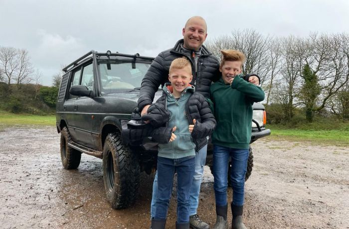 a man and two young boys standing in front of a 4 x 4 vehicle as part of a driving experience
