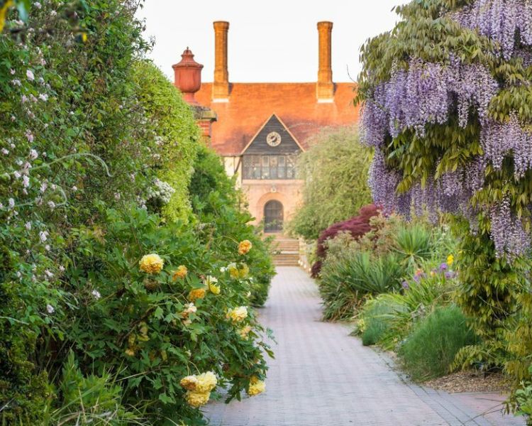 a walkway through the gardens at rhs wisley leading up to the main house