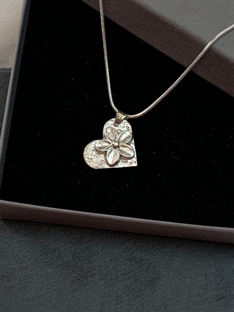 a heart shaped pendant with a flower in the middle made out of silver clay on a taster workshop
