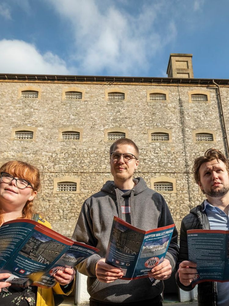 three young people standing outside a former prison looking at maps on a self guided tour