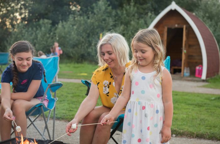 Family time toasting marshmallow in campfire camping pod holiday