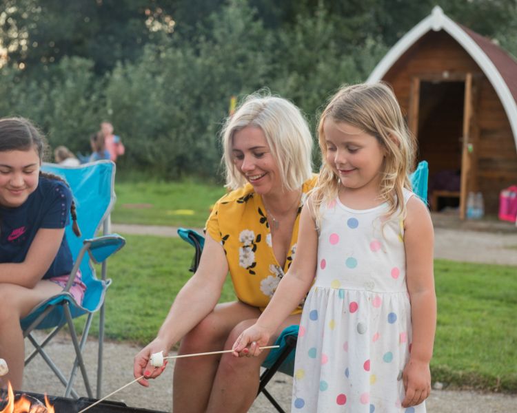 Family time toasting marshmallow in campfire camping pod holiday