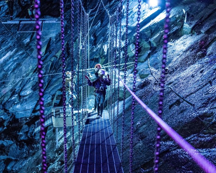 people walking along a swing bridge underground in zip world caverns